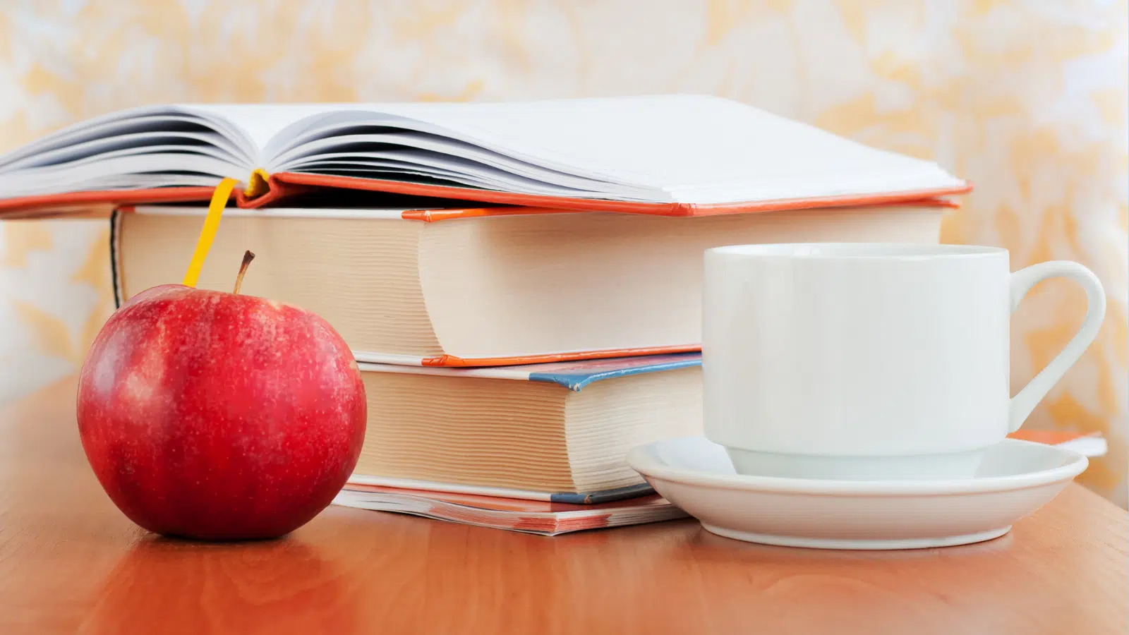 A stack of books with an apple and a coffee cup